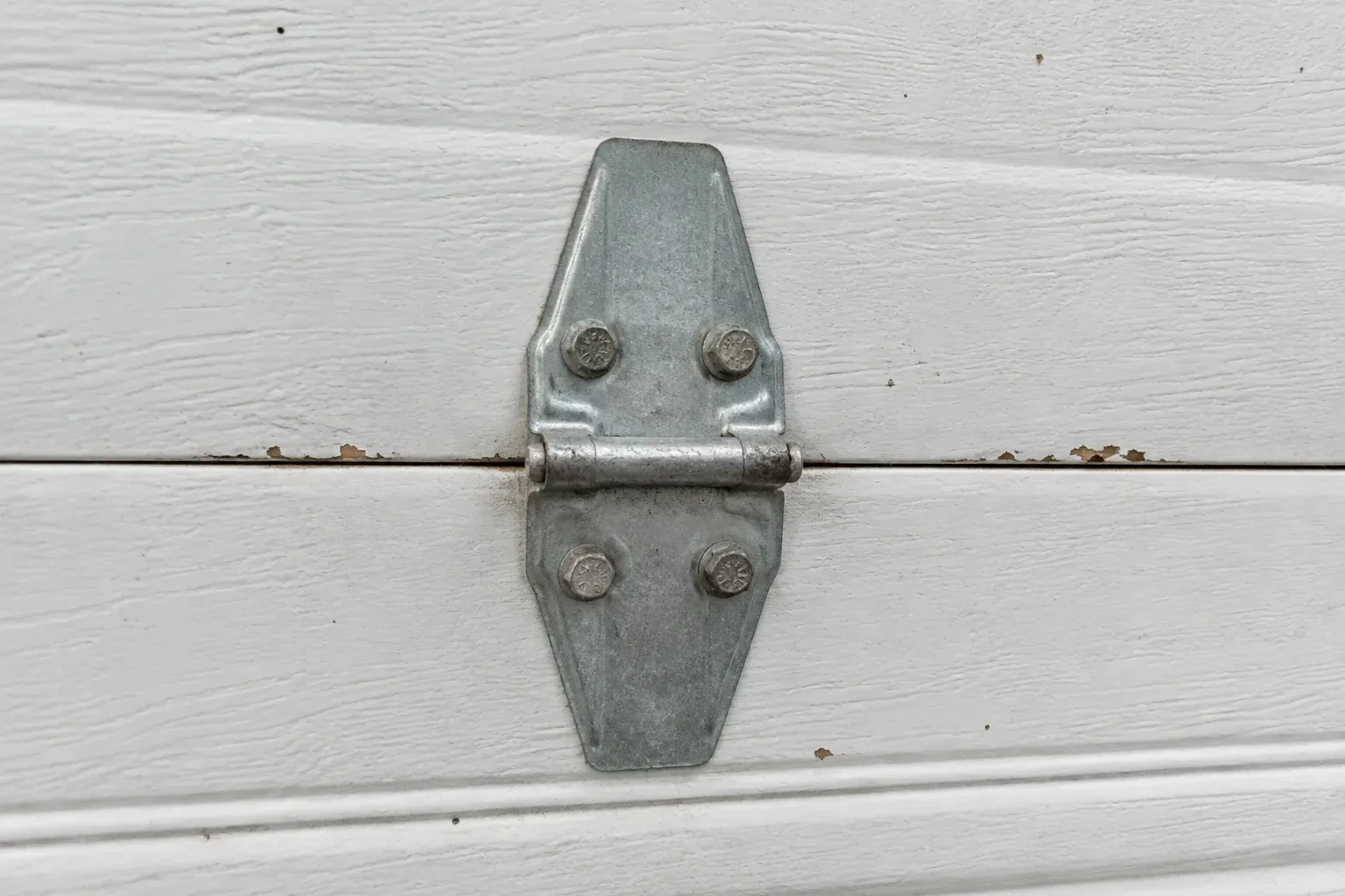 Metal center hinge across a seam in a white sectional garage door. — Garage Door Hinge Replacement, Wasaga Beach