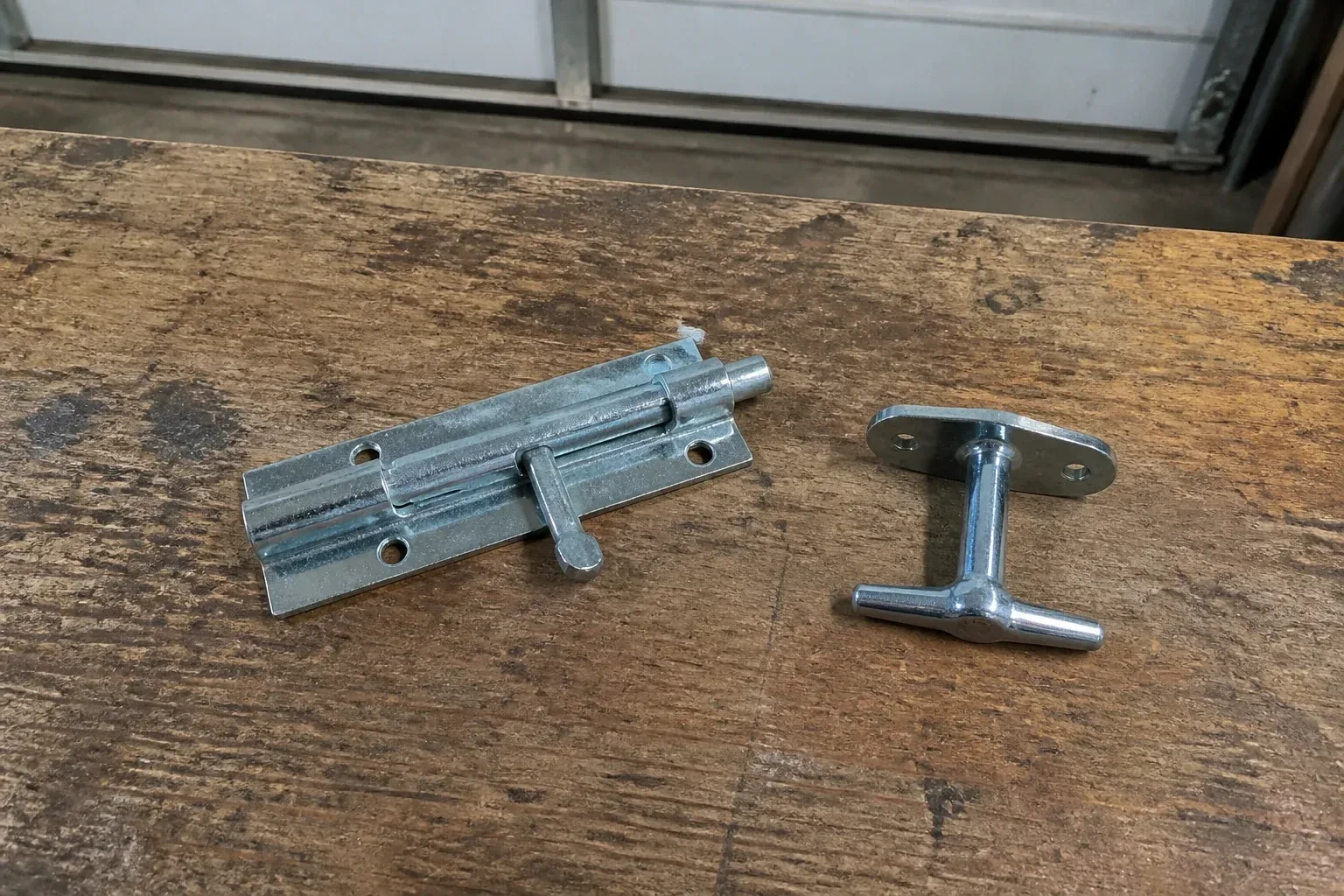 Detached slide bolt and T-handle on a wooden garage workbench. — Garage Door Manual Lock Repair, Wasaga Beach